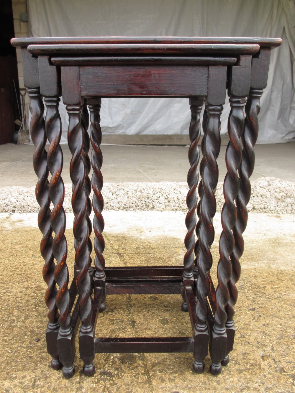 A nest of three dark oak square-topped side tables featuring carved barley twist legs and low stretchers.