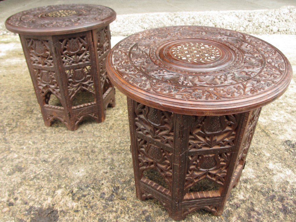 A pair of 19th-century Anglo-Indian padauk wood occasional tables featuring circular tops with deep foliate carvings and central bone inlay set upon collapsible octagonal pierced fretwork bases.