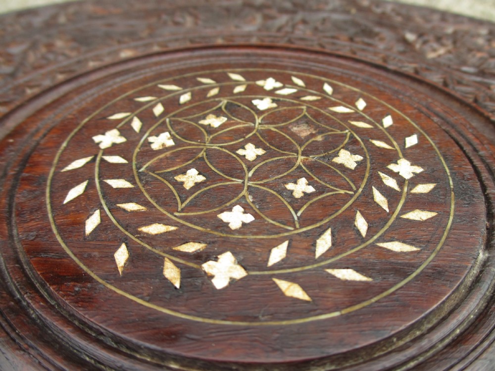 A pair of 19th-century Anglo-Indian padauk wood occasional tables featuring circular tops with deep foliate carvings and central bone inlay set upon collapsible octagonal pierced fretwork bases. View X