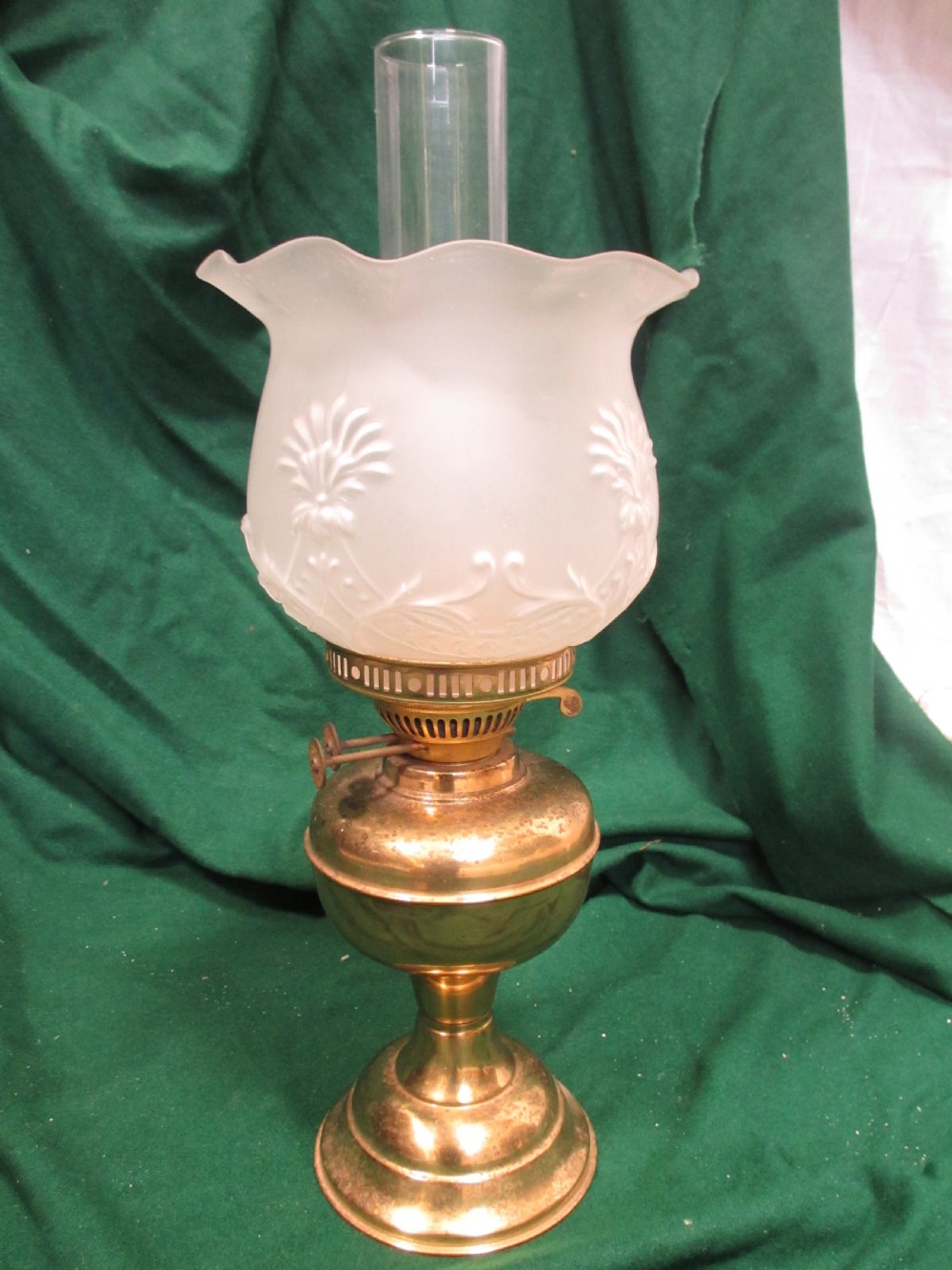A Victorian oil lamp featuring a brass pedestal base and reservoir, a frosted glass shade with a frilled rim and floral relief patterns, and a clear glass chimney.