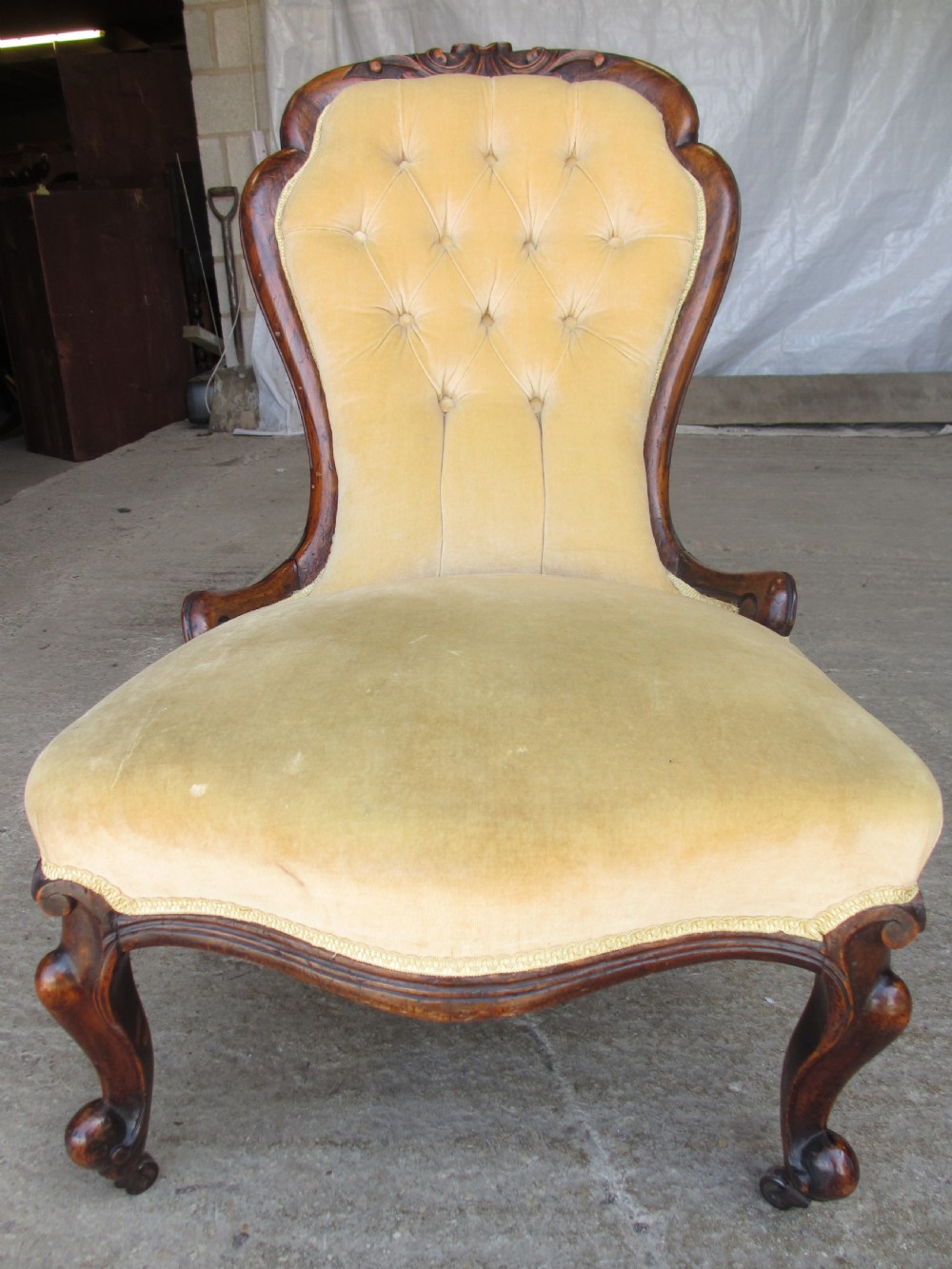 A Victorian spoon back nursing chair featuring yellow velvet button-tufted upholstery and a carved mahogany frame with cabriole legs.