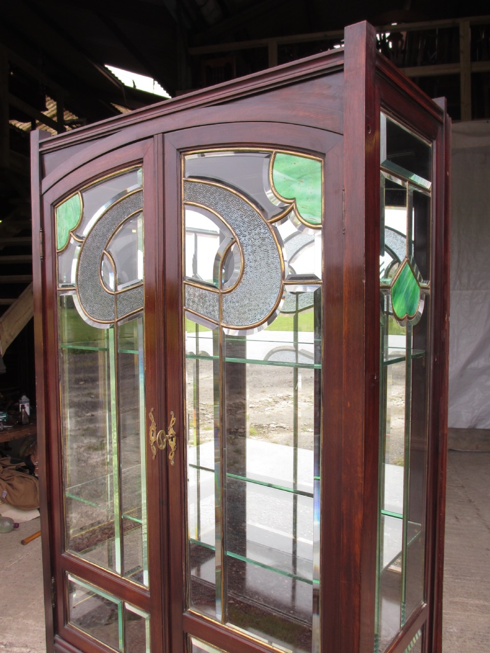 A late 19th-century mahogany Art Nouveau display cabinet featuring leaded glass doors with green accents, stylized glazing bars, interior glass shelving, and a lower open undertier. View XII