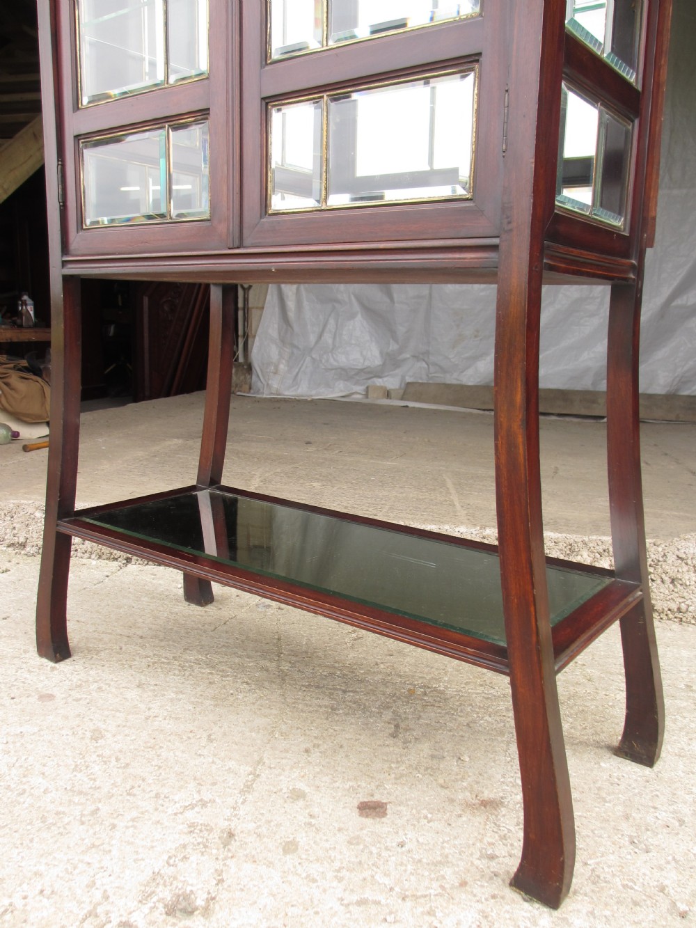 A late 19th-century mahogany Art Nouveau display cabinet featuring leaded glass doors with green accents, stylized glazing bars, interior glass shelving, and a lower open undertier. View II