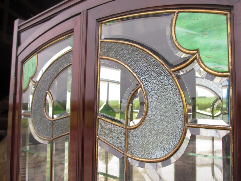 A late 19th-century mahogany Art Nouveau display cabinet featuring leaded glass doors with green accents, stylized glazing bars, interior glass shelving, and a lower open undertier. View III