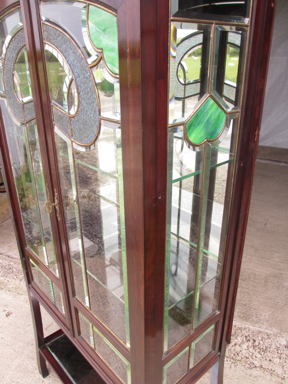 A late 19th-century mahogany Art Nouveau display cabinet featuring leaded glass doors with green accents, stylized glazing bars, interior glass shelving, and a lower open undertier. View V