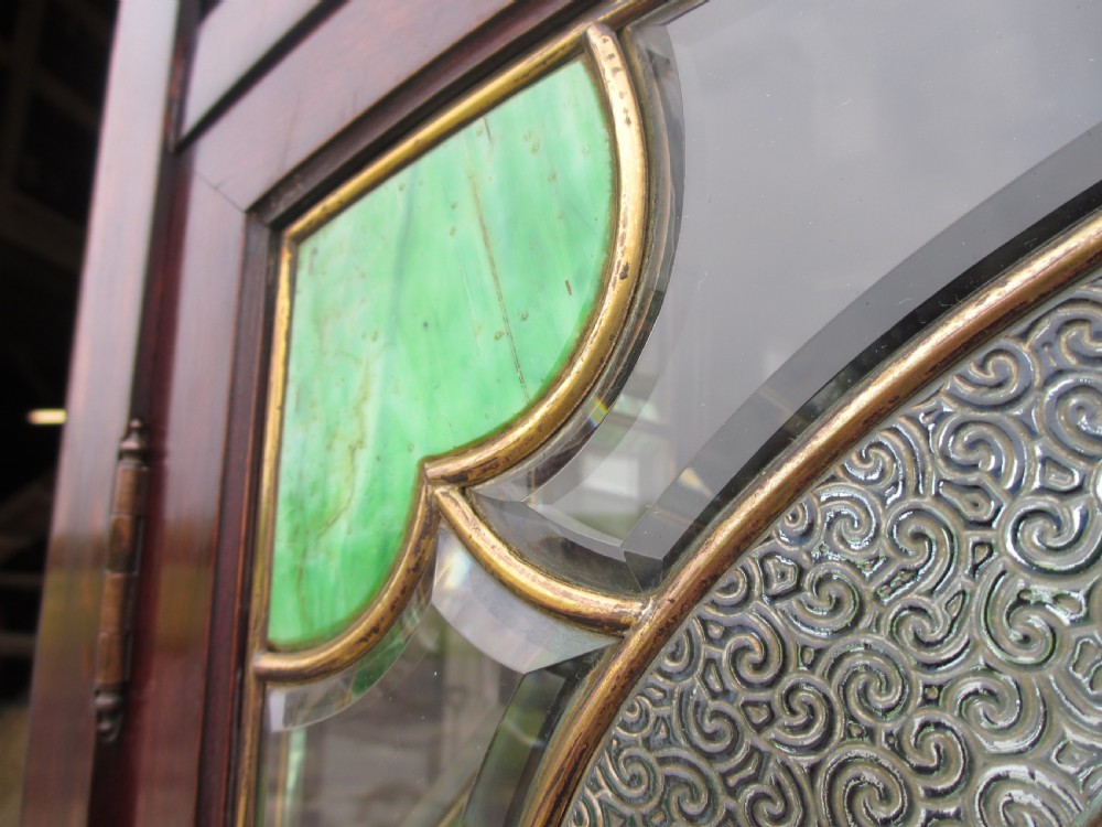 A late 19th-century mahogany Art Nouveau display cabinet featuring leaded glass doors with green accents, stylized glazing bars, interior glass shelving, and a lower open undertier. View VI