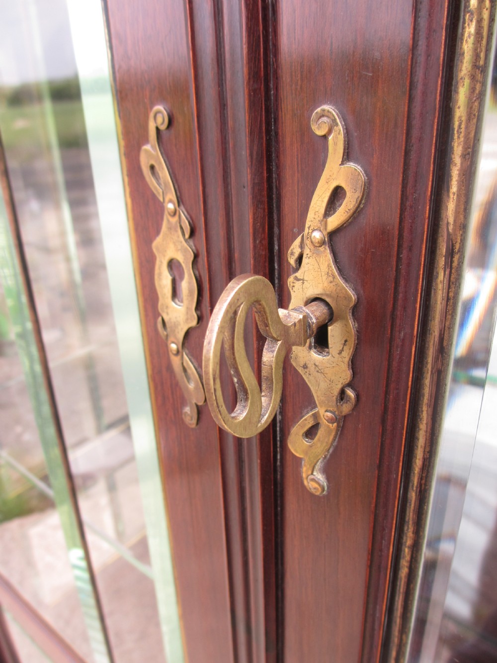 A late 19th-century mahogany Art Nouveau display cabinet featuring leaded glass doors with green accents, stylized glazing bars, interior glass shelving, and a lower open undertier. View VII