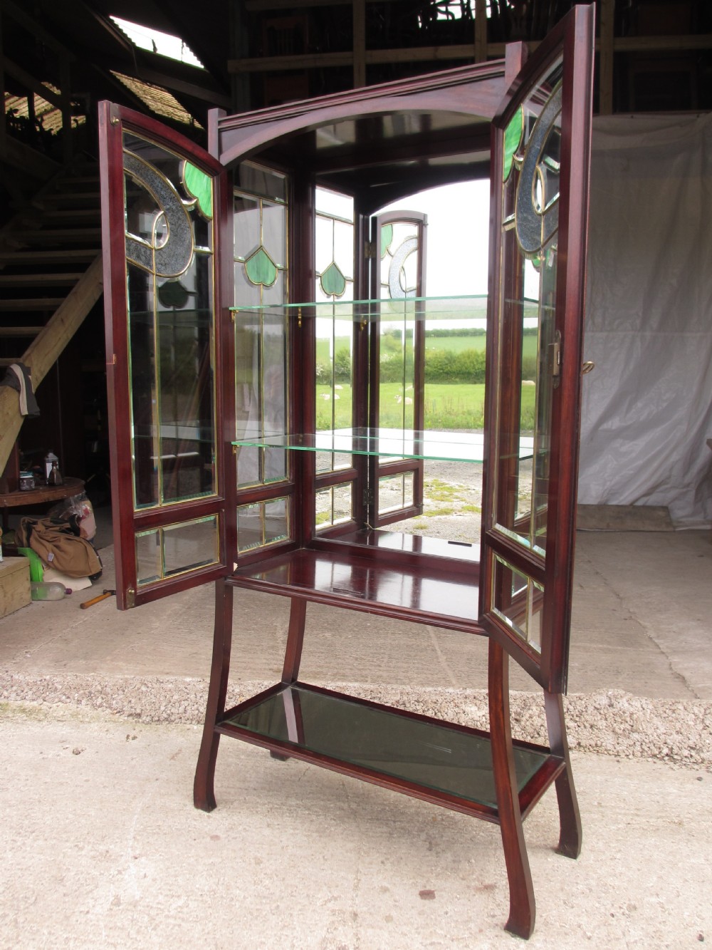 A late 19th-century mahogany Art Nouveau display cabinet featuring leaded glass doors with green accents, stylized glazing bars, interior glass shelving, and a lower open undertier. View VIII