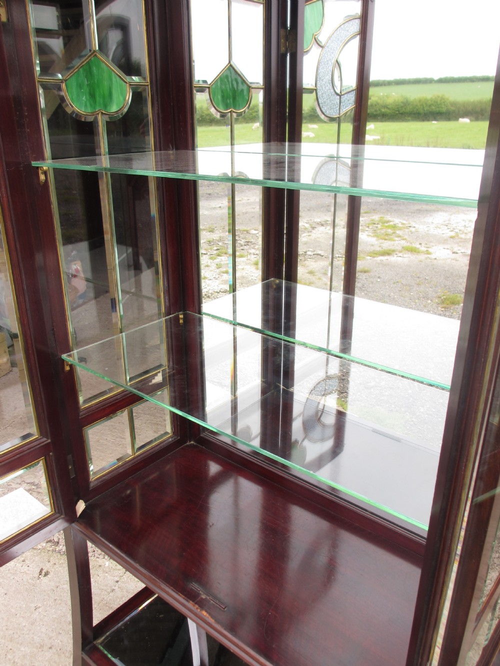 A late 19th-century mahogany Art Nouveau display cabinet featuring leaded glass doors with green accents, stylized glazing bars, interior glass shelving, and a lower open undertier. View IX