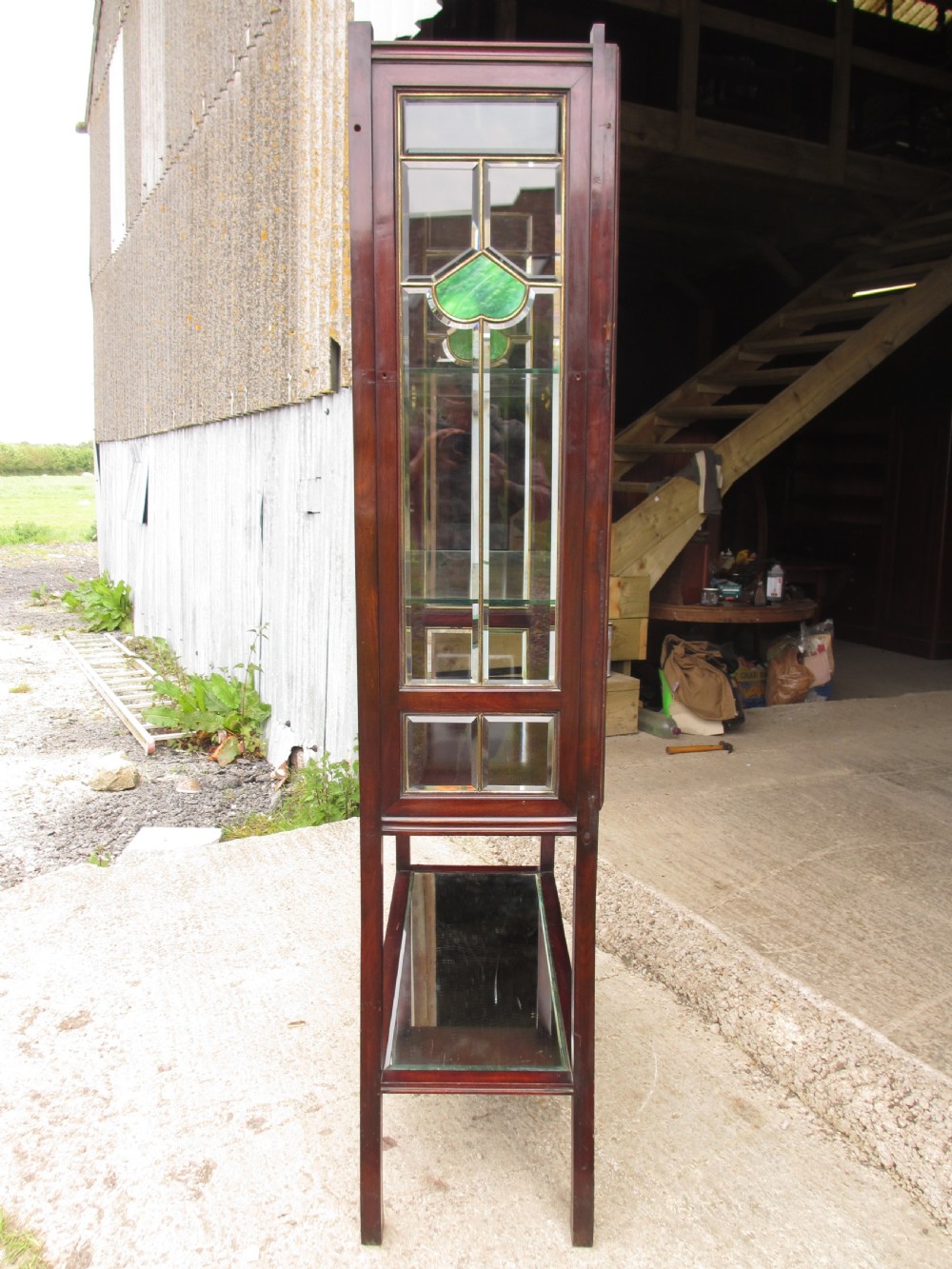 A late 19th-century mahogany Art Nouveau display cabinet featuring leaded glass doors with green accents, stylized glazing bars, interior glass shelving, and a lower open undertier. View X
