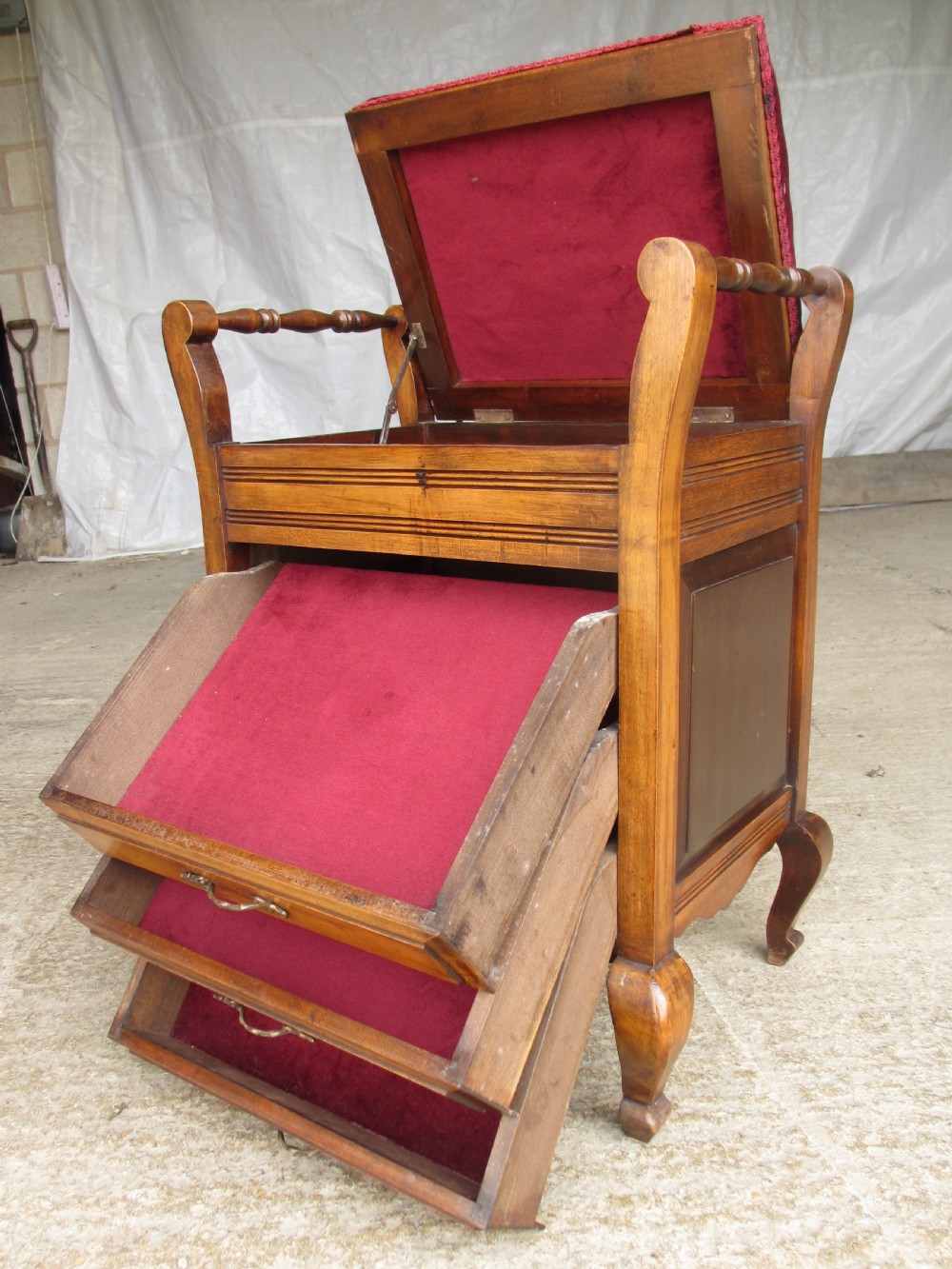 An Edwardian mahogany music stool featuring a red velvet upholstered seat, side turned handles, brass drawer pulls, and cabriole legs. View II