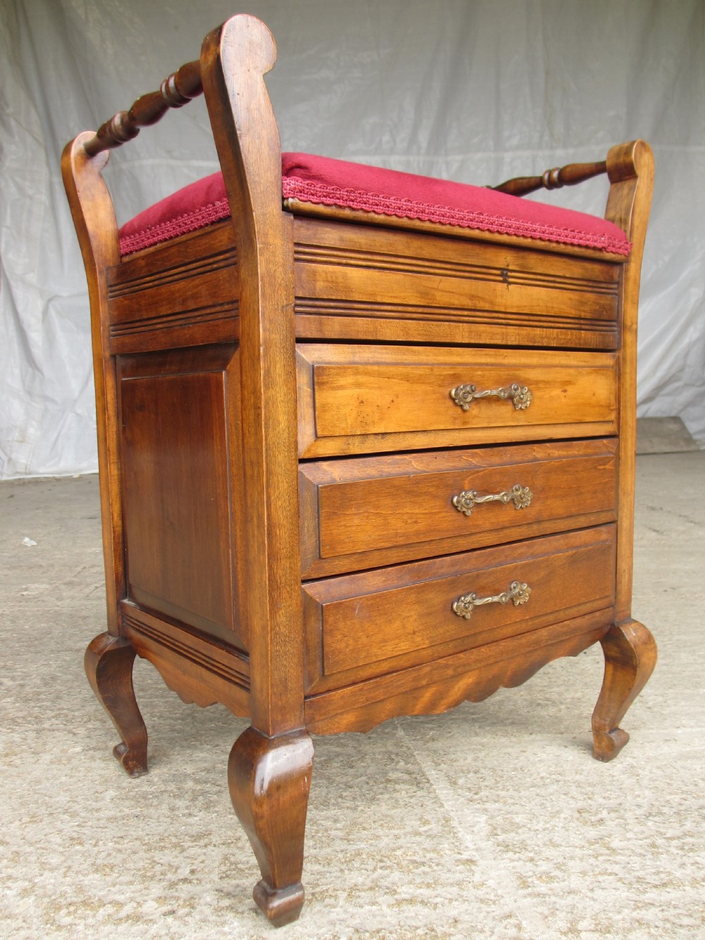 An Edwardian mahogany music stool featuring a red velvet upholstered seat, side turned handles, brass drawer pulls, and cabriole legs. View III