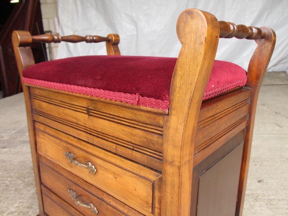 An Edwardian mahogany music stool featuring a red velvet upholstered seat, side turned handles, brass drawer pulls, and cabriole legs. View IV