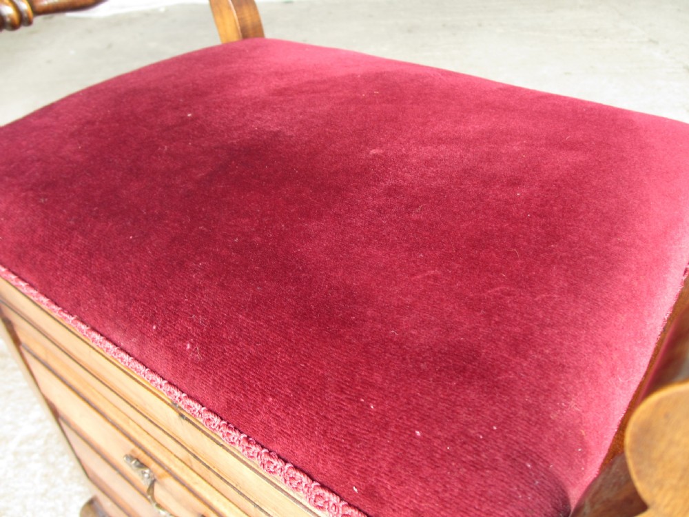 An Edwardian mahogany music stool featuring a red velvet upholstered seat, side turned handles, brass drawer pulls, and cabriole legs. View V