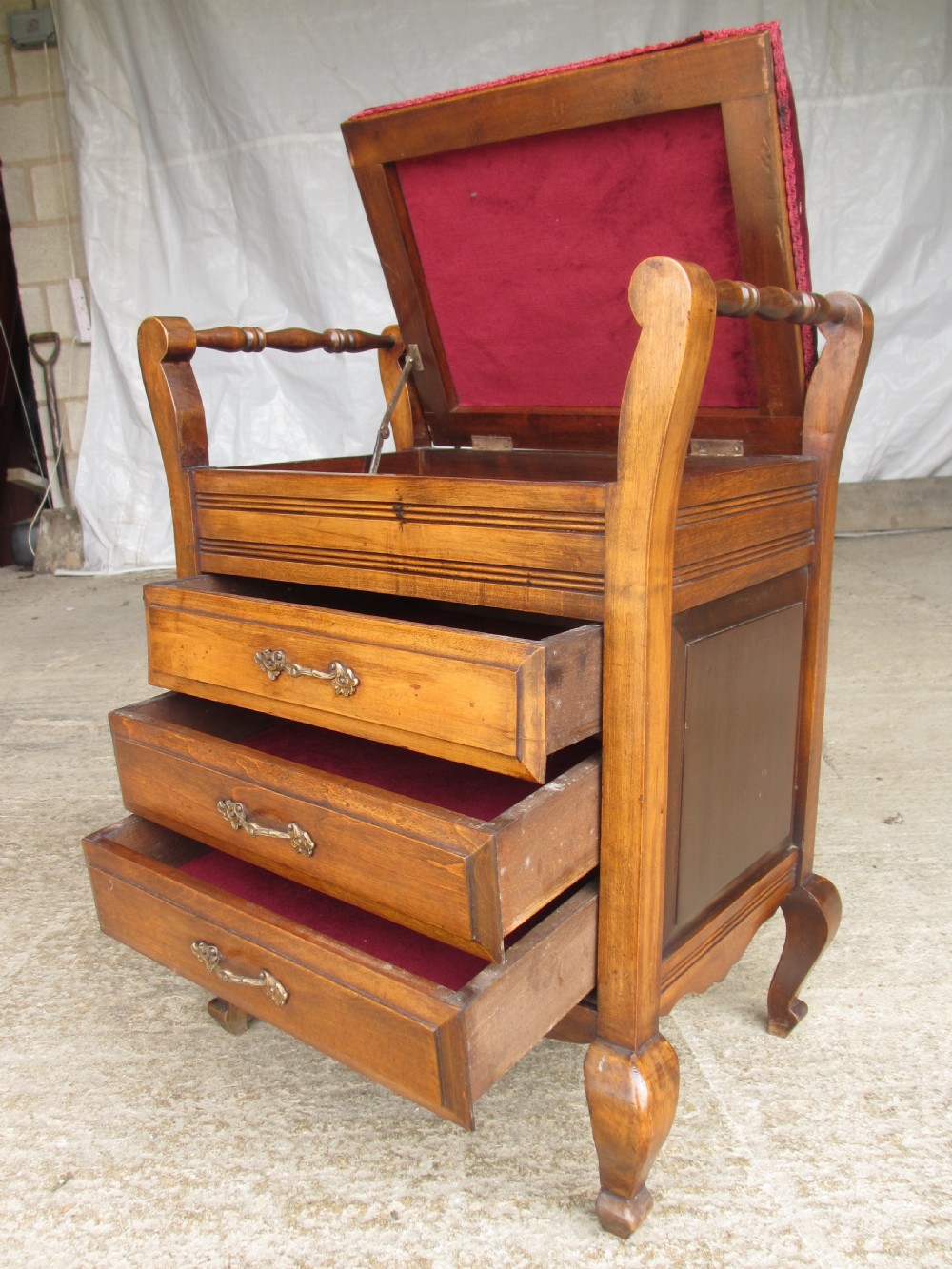 An Edwardian mahogany music stool featuring a red velvet upholstered seat, side turned handles, brass drawer pulls, and cabriole legs. View VIII
