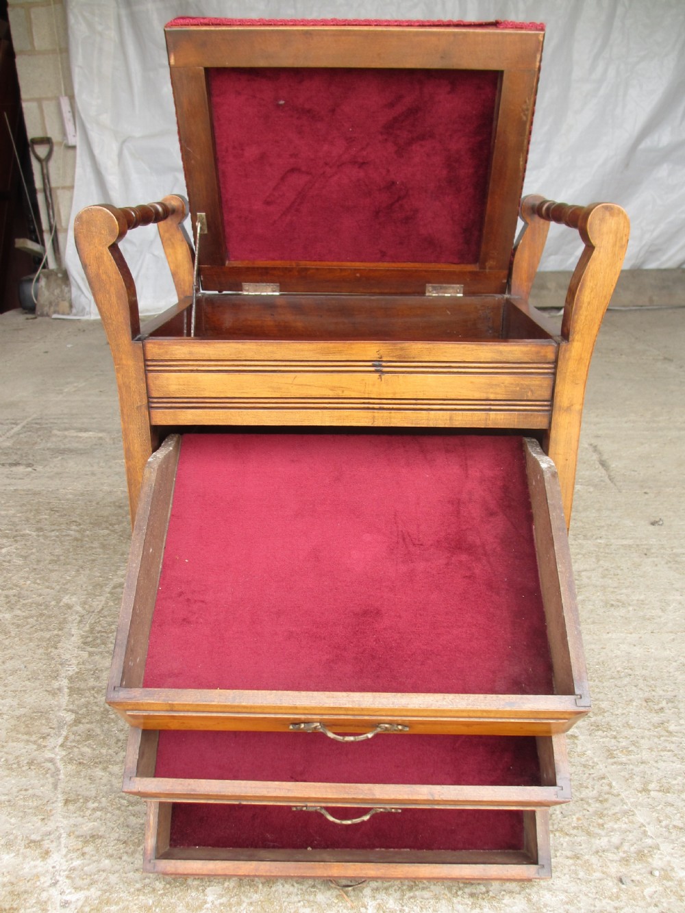 An Edwardian mahogany music stool featuring a red velvet upholstered seat, side turned handles, brass drawer pulls, and cabriole legs. View X