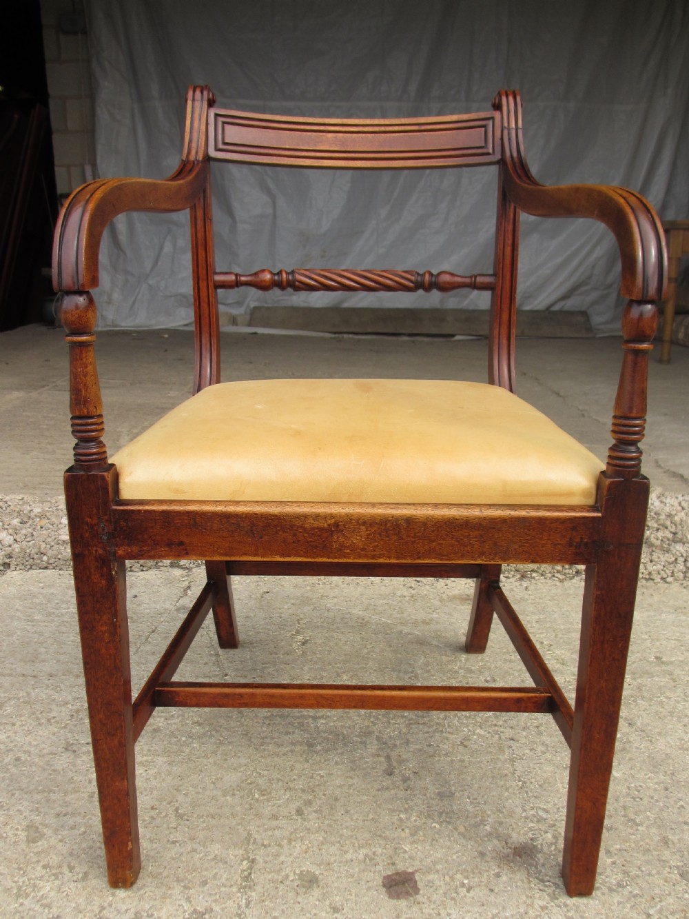 A Georgian mahogany armchair featuring curved reeded arms, a carved rope-twist horizontal back bar, turned front supports, and a tan drop-in upholstered seat.