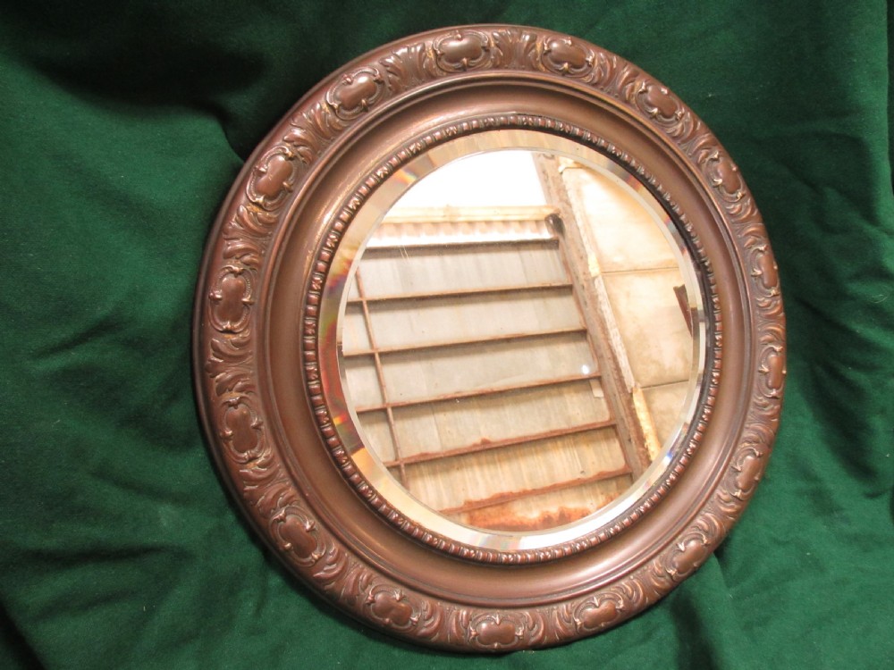A circular Victorian brass wall mirror featuring an embossed floral patterned frame and a bevelled glass mirror plate.