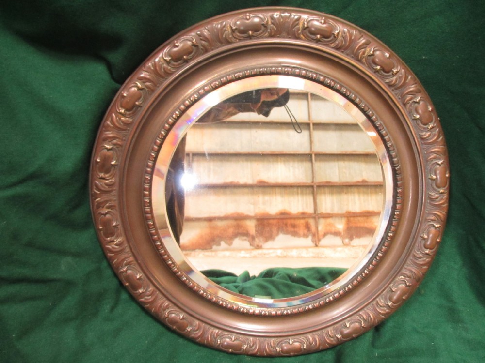A circular Victorian brass wall mirror featuring an embossed floral patterned frame and a bevelled glass mirror plate. View II