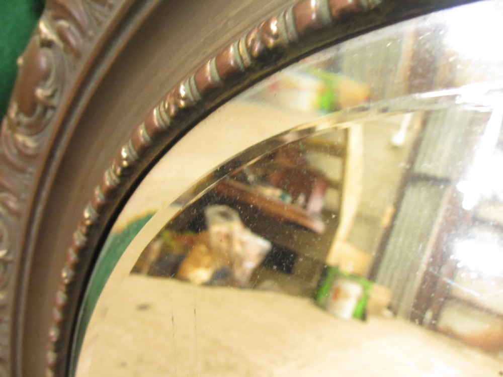 A circular Victorian brass wall mirror featuring an embossed floral patterned frame and a bevelled glass mirror plate. View III