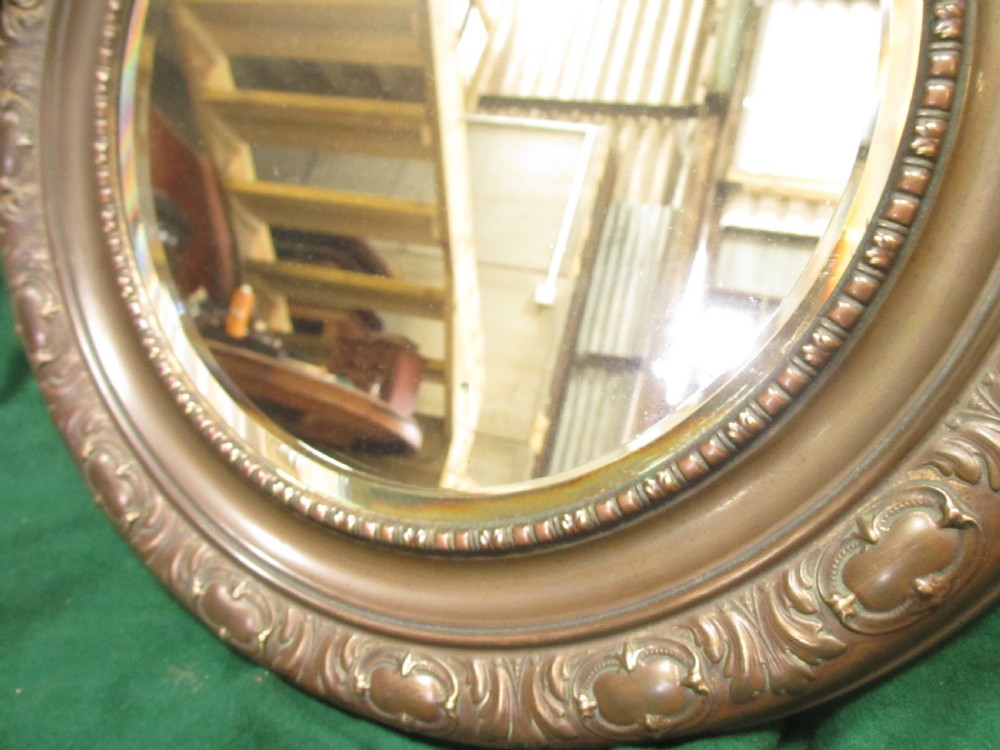 A circular Victorian brass wall mirror featuring an embossed floral patterned frame and a bevelled glass mirror plate. View V