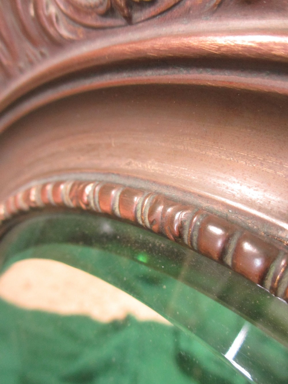 A circular Victorian brass wall mirror featuring an embossed floral patterned frame and a bevelled glass mirror plate. View VI