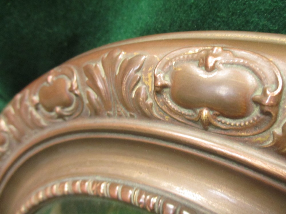 A circular Victorian brass wall mirror featuring an embossed floral patterned frame and a bevelled glass mirror plate. View VII