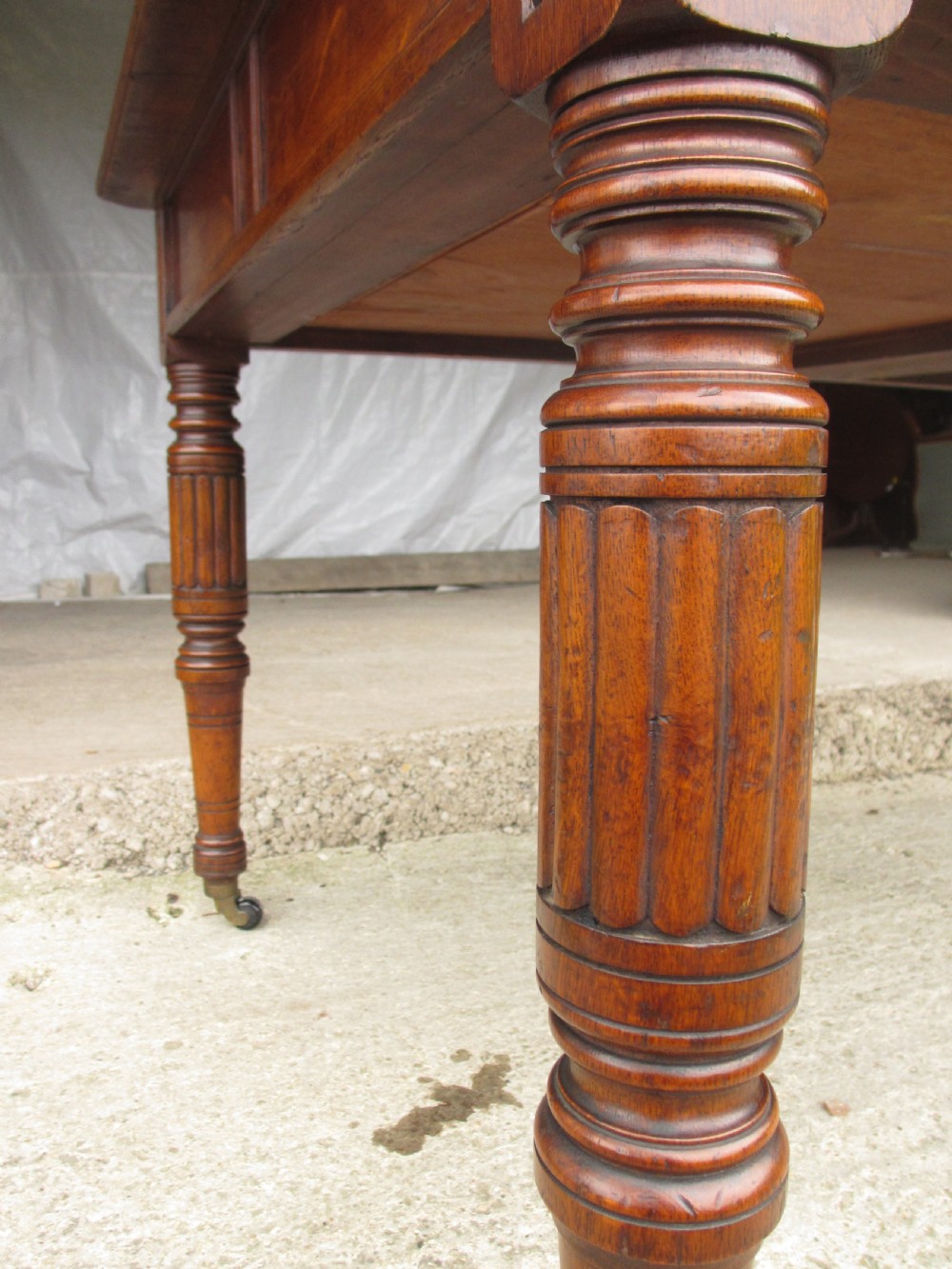 An Edwardian Arts and Crafts warm brown oak library table featuring two front drawers, a carved central floral panel, turned legs, and brass handles on castors. View V