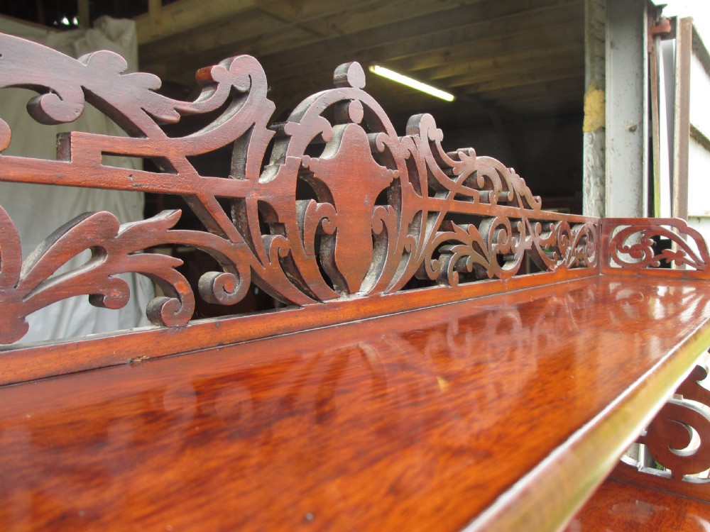 A Victorian mahogany chiffonier featuring two lower cupboard doors with figured plum pudding veneer panels, topped with two open display shelves supported by carved scroll brackets and a fretwork cresting. View IV