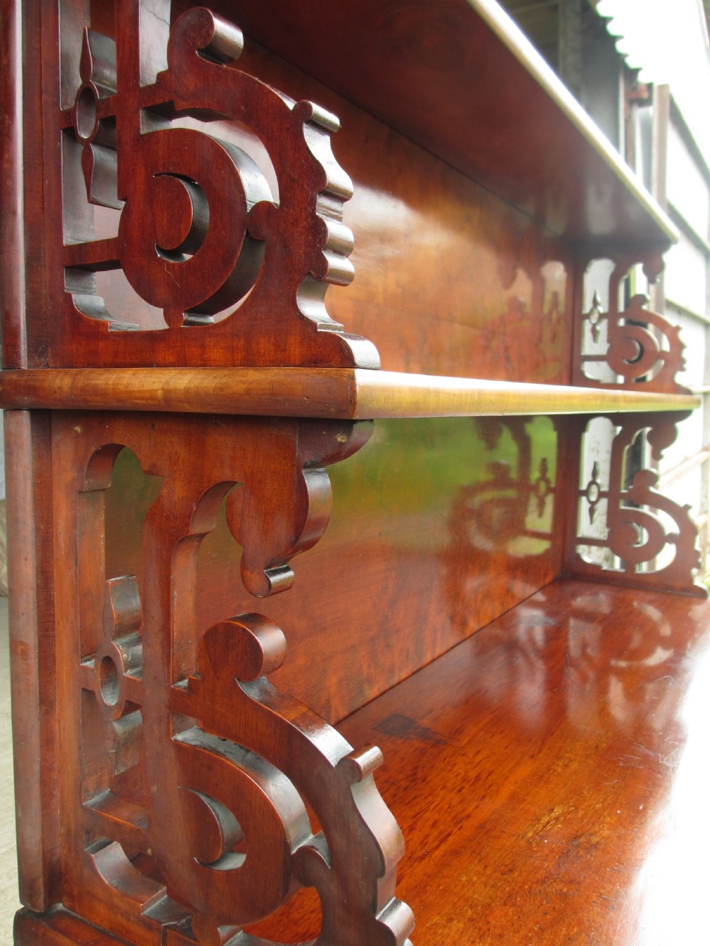 A Victorian mahogany chiffonier featuring two lower cupboard doors with figured plum pudding veneer panels, topped with two open display shelves supported by carved scroll brackets and a fretwork cresting. View V