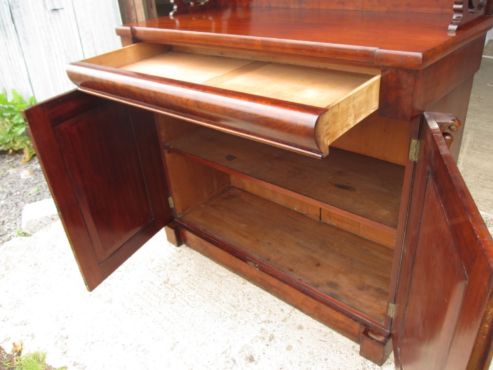A Victorian mahogany chiffonier featuring two lower cupboard doors with figured plum pudding veneer panels, topped with two open display shelves supported by carved scroll brackets and a fretwork cresting. View IX
