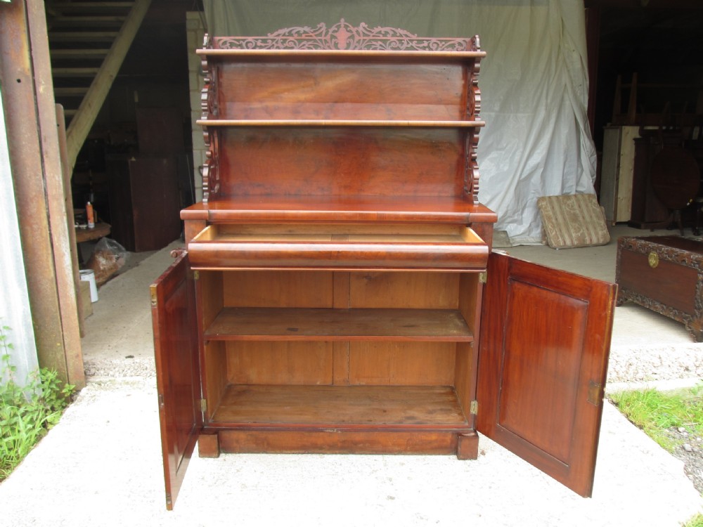 A Victorian mahogany chiffonier featuring two lower cupboard doors with figured plum pudding veneer panels, topped with two open display shelves supported by carved scroll brackets and a fretwork cresting. View X