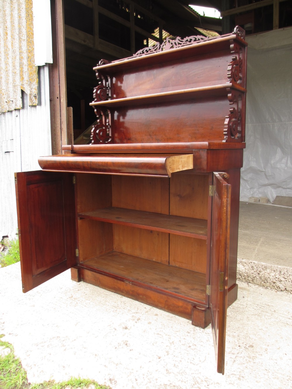 A Victorian mahogany chiffonier featuring two lower cupboard doors with figured plum pudding veneer panels, topped with two open display shelves supported by carved scroll brackets and a fretwork cresting. View XI