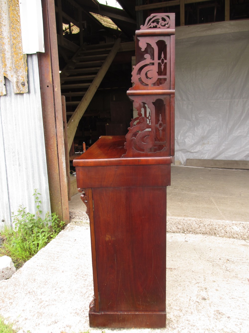 A Victorian mahogany chiffonier featuring two lower cupboard doors with figured plum pudding veneer panels, topped with two open display shelves supported by carved scroll brackets and a fretwork cresting. View XII