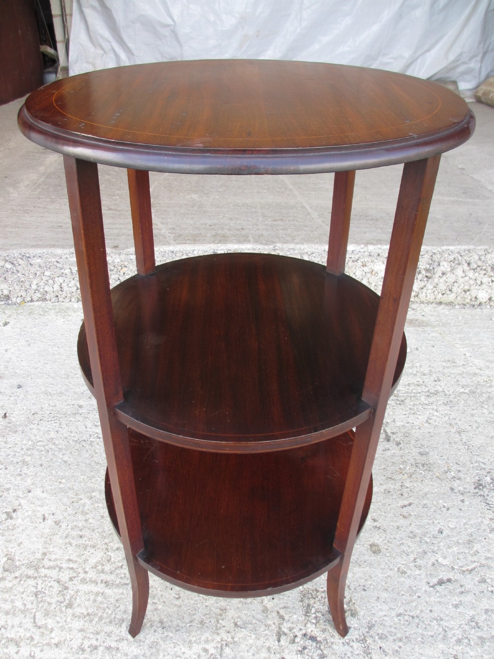 An Edwardian circular dark mahogany etagere featuring three tiers supported by four slender legs with inlaid edge detailing. View X