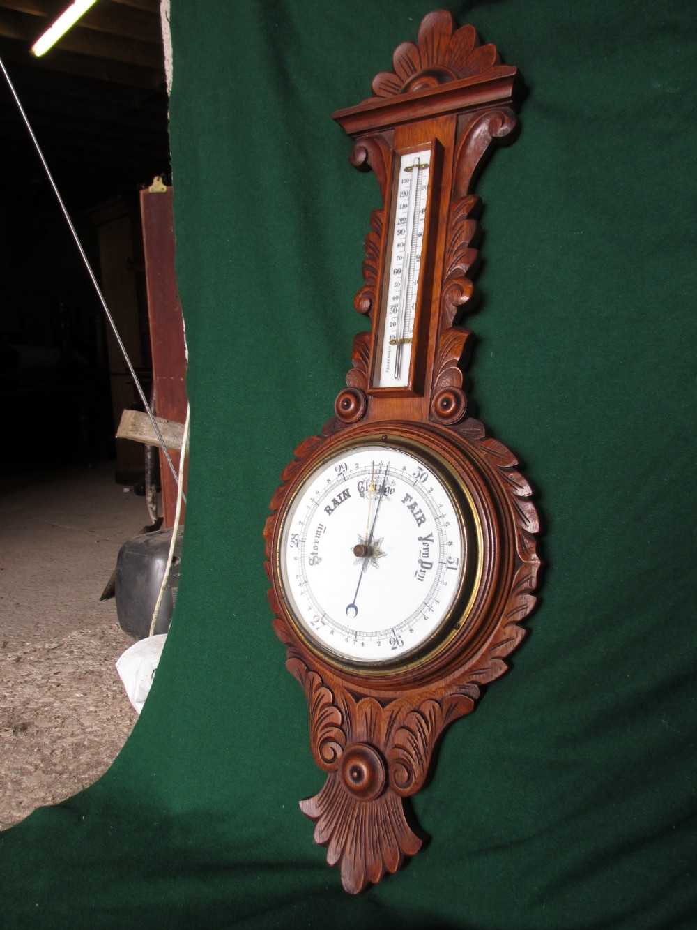 A Victorian carved oak wall barometer featuring an upper thermometer, intricate leaf scrollwork motifs, and a circular white dial with a brass bezel. View III