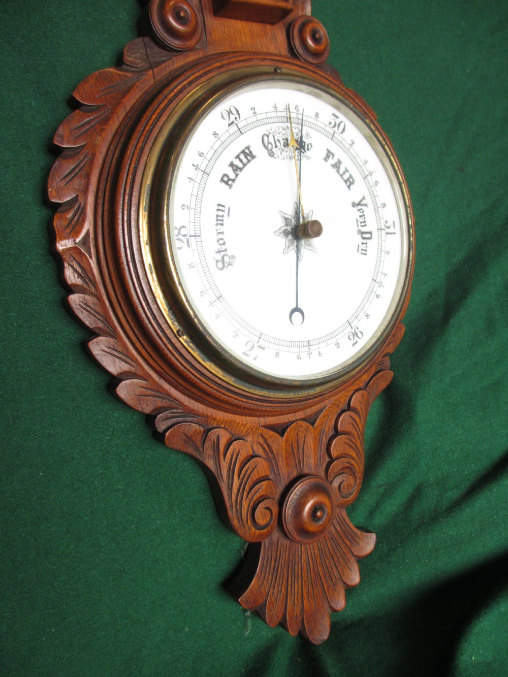 A Victorian carved oak wall barometer featuring an upper thermometer, intricate leaf scrollwork motifs, and a circular white dial with a brass bezel. View V