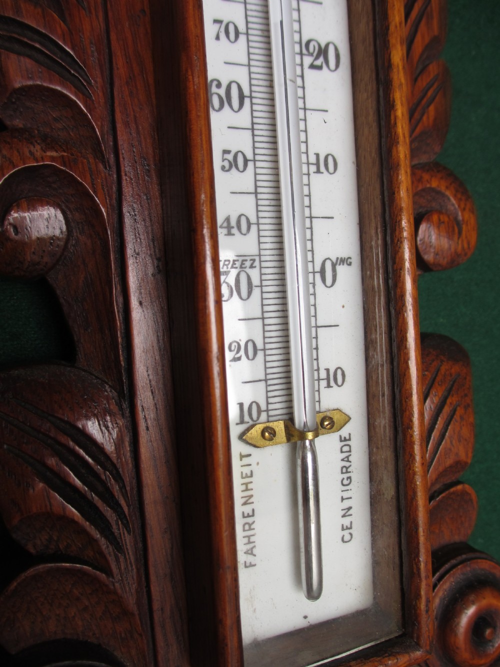 A Victorian carved oak wall barometer featuring an upper thermometer, intricate leaf scrollwork motifs, and a circular white dial with a brass bezel. View VI