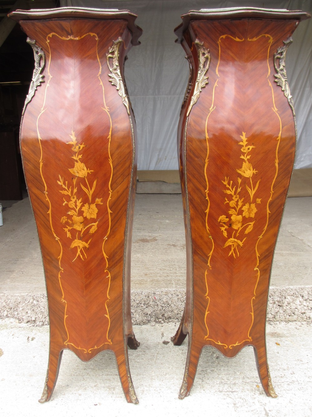 A pair of tall French Louis XV style wooden pedestals featuring floral marquetry inlays, curved silhouettes, and decorative gilt-bronze mounts.