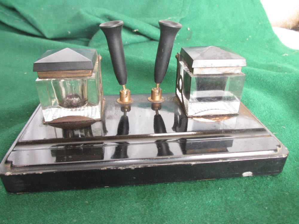 A Victorian inkstand featuring a black base with a front pen groove, two upright trumpet pen rests, and two square glass inkwells with dark lids. View III