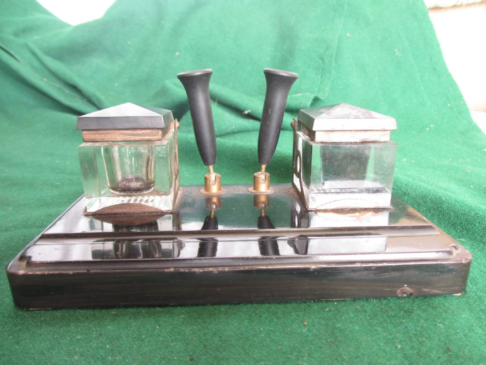 A Victorian inkstand featuring a black base with a front pen groove, two upright trumpet pen rests, and two square glass inkwells with dark lids. View II