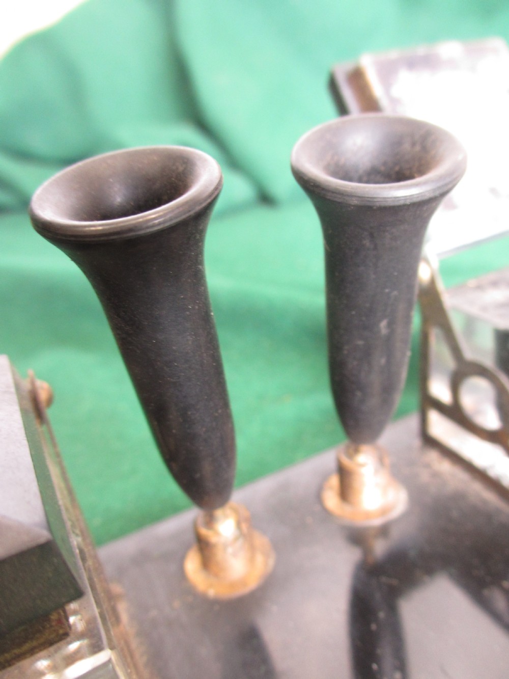 A Victorian inkstand featuring a black base with a front pen groove, two upright trumpet pen rests, and two square glass inkwells with dark lids. View VII