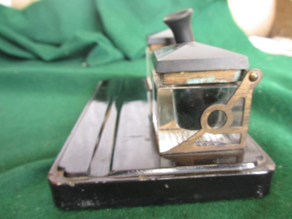 A Victorian inkstand featuring a black base with a front pen groove, two upright trumpet pen rests, and two square glass inkwells with dark lids. View X