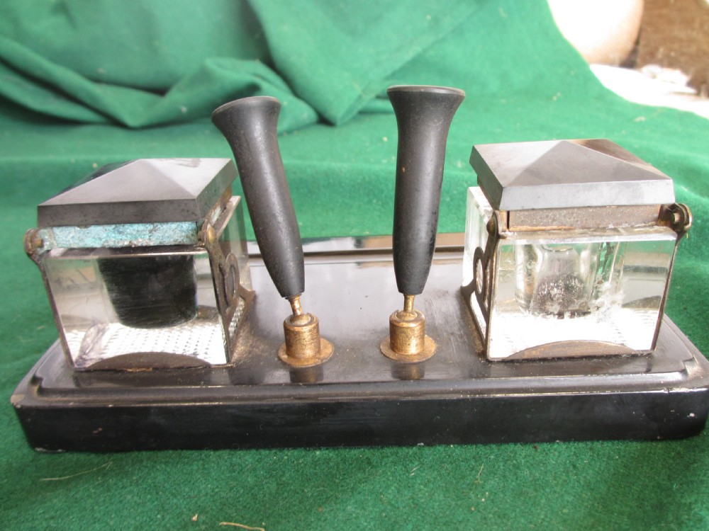 A Victorian inkstand featuring a black base with a front pen groove, two upright trumpet pen rests, and two square glass inkwells with dark lids. View XI