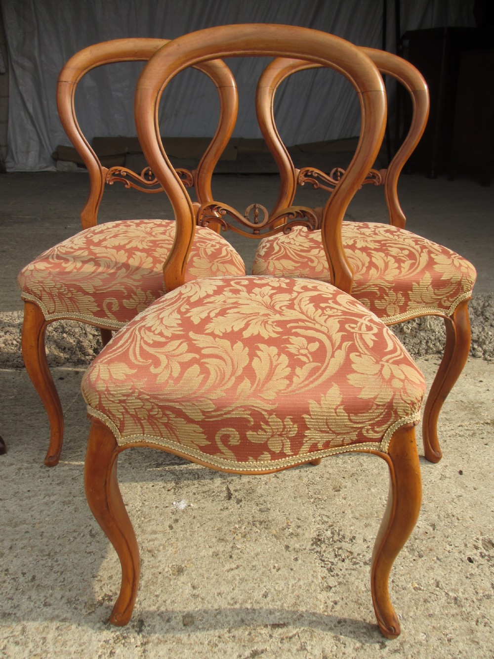 A set of three Victorian mahogany dining chairs featuring rounded balloon backs, carved central splats, cabriole front legs, and terracotta floral upholstery.