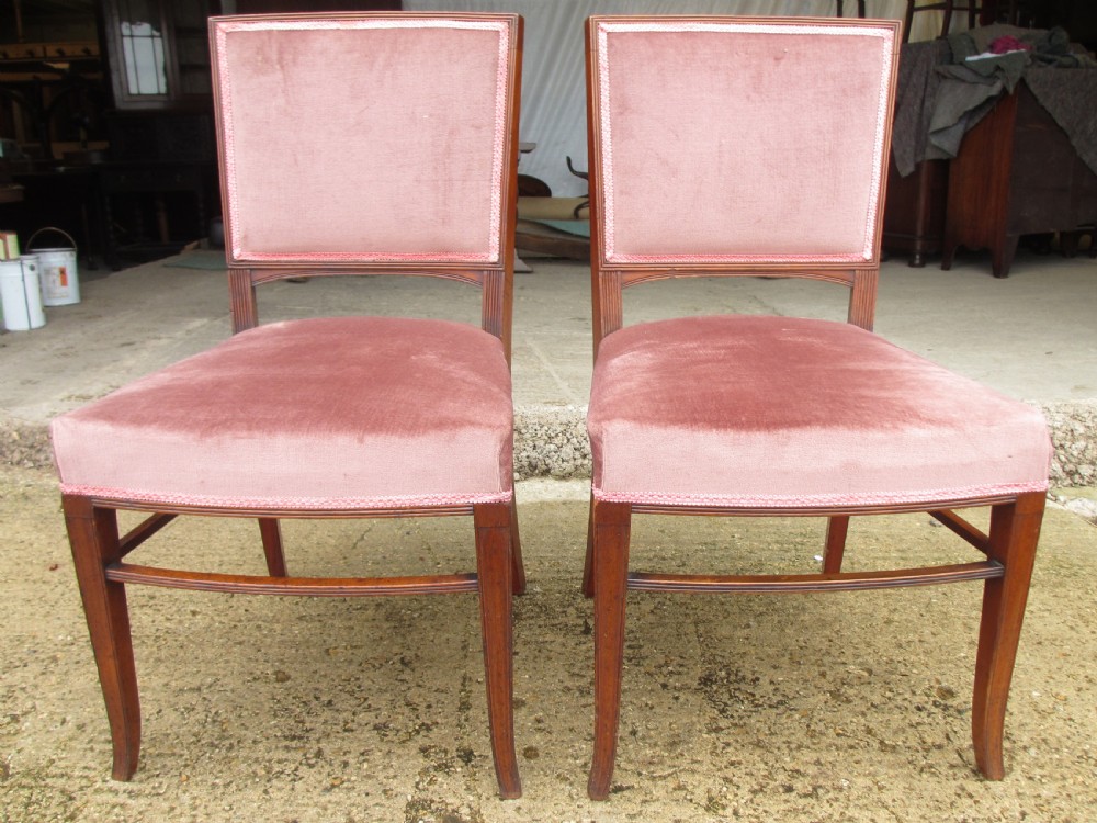 A pair of 19th-century mahogany dining chairs featuring upholstered dusty pink velvet rectangular backs and seats with reeded wooden legs.