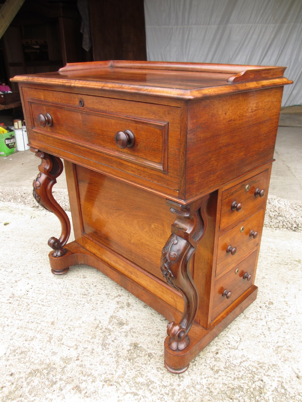 A Victorian rosewood davenport secretaire desk featuring an open black leather-lined writing slope, an upper gallery with drawers and pigeonholes, side drawers, and carved cabriole supports. View IV