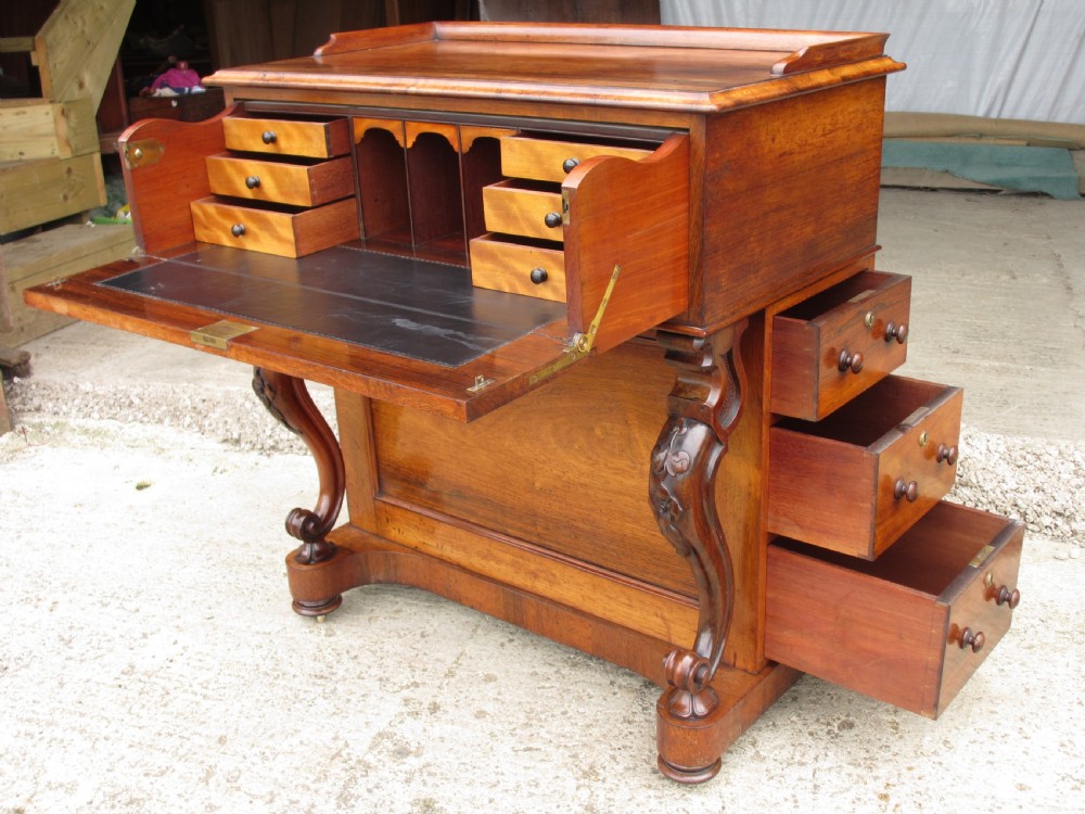 A Victorian rosewood davenport secretaire desk featuring an open black leather-lined writing slope, an upper gallery with drawers and pigeonholes, side drawers, and carved cabriole supports. View X