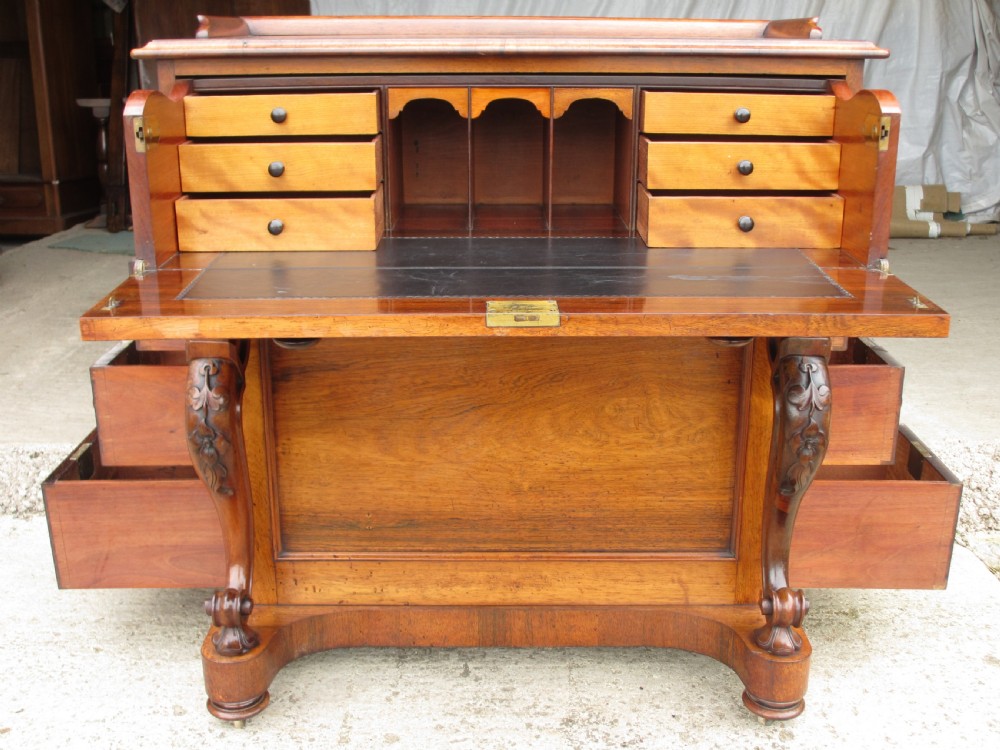 A Victorian rosewood davenport secretaire desk featuring an open black leather-lined writing slope, an upper gallery with drawers and pigeonholes, side drawers, and carved cabriole supports.
