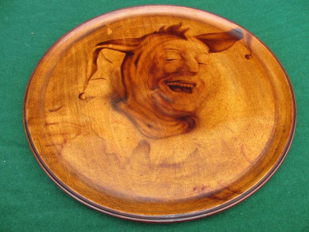 A circular turned mahogany wooden tray featuring a central branded portrait of a laughing jester wearing a cap with bells.